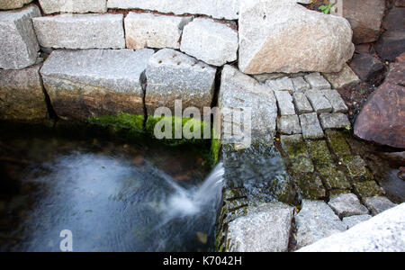 a flowing small waterfall beside green algae growing on white stones Stock Photo
