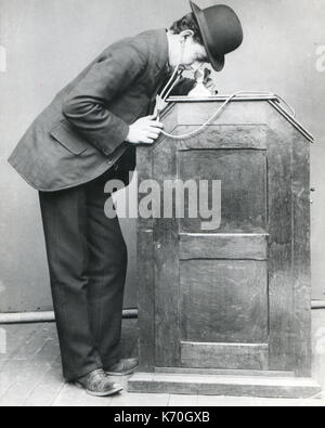 New York - A man looking into the Edison 'peep-hole' Kinetoscope. It is equipped with hearing tubes for synchronized sound. This was the first important motion-picture exhibiting machine. Stock Photo