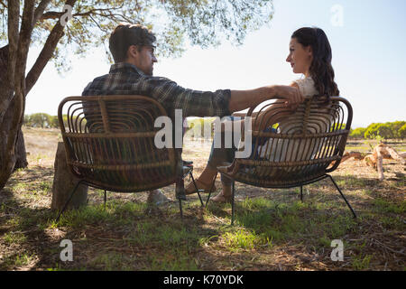 Young couple looking each other while sitting on chairs at field Stock Photo