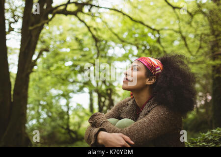 Thoughtful young woman sitting by tree at forest Stock Photo