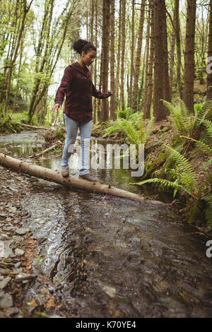 Full length of young woman balancing on fallen tree at forest Stock Photo