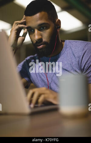 Young man listening music while using laptop at table in cafe Stock Photo