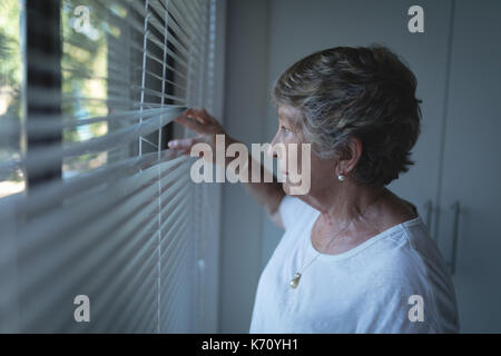 Senior woman looking through window at home Stock Photo