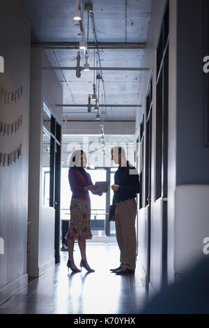 Businesswoman with colleague discussing over document in corridor at office Stock Photo