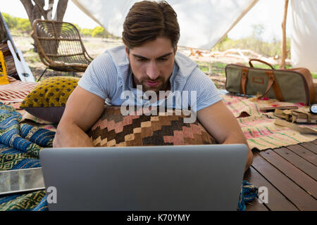 Relaxed young man using laptop while lying down in tent Stock Photo