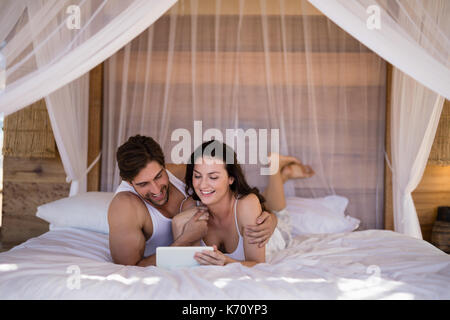 Smiling couple using digital tablet on bed in cottage Stock Photo