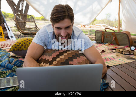 Relaxed smiling man using laptop while lying down in tent Stock Photo