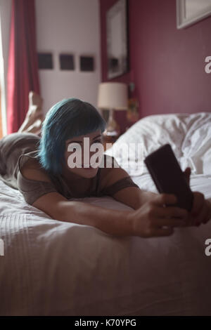Young woman using phone while lying on bed at home Stock Photo