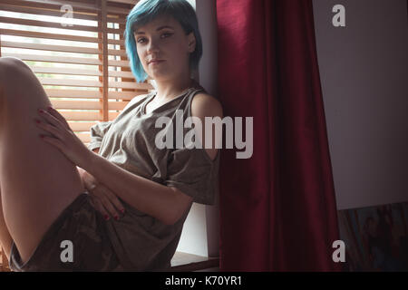 Portrait of young woman sitting by window in bedroom at home Stock Photo