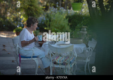 Senior woman using laptop while having coffee in garden Stock Photo