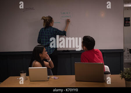 Colleagues looking at businesswoman writing on whiteboard in office Stock Photo