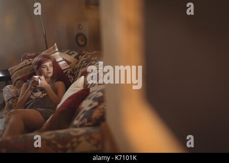 Young woman having coffee while lying on sofa at home Stock Photo