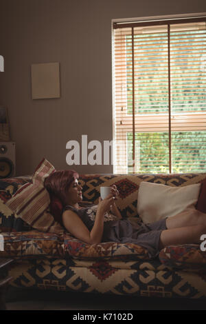 Side view of young woman having coffee on sofa at home Stock Photo