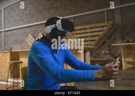 Man using mobile phone while looking through virtual reality in cafeteria Stock Photo