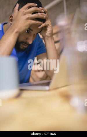 Frustrated young man with laptop sitting at table in cafeteria Stock Photo