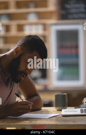 Close up of young man writing while sitting with laptop in cafe Stock Photo