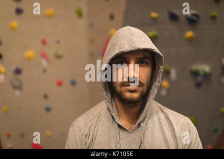 Portrait of male athlete wearing hooded shirt while standing by climbing wall in gym Stock Photo