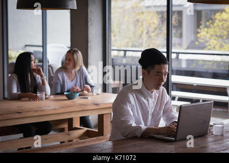Businessman using laptop with colleagues discussing at table in office cafeteria Stock Photo