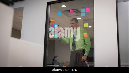 Businessman writing on sticky note seen through glass in office Stock Photo