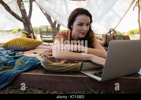 Young woman using laptop on plank in tent Stock Photo