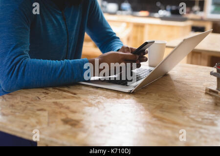 Midsection of young man using mobile phone while sitting in cafe Stock Photo