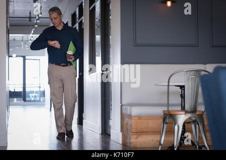 Businessman checking time while walking in corridor at office Stock Photo