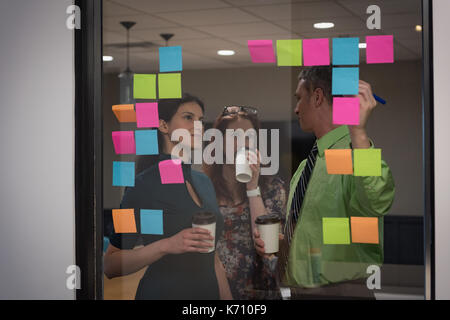 Business people discussing over sticky notes seen through glass in office Stock Photo