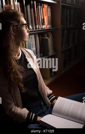 Thoughtful woman sitting with book in library room Stock Photo