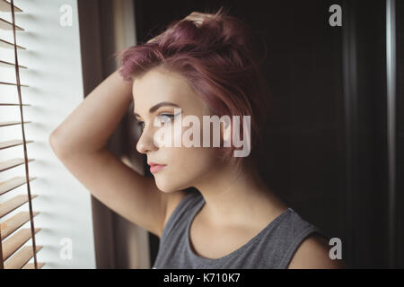 Thoughtful young woman looking through window at home Stock Photo