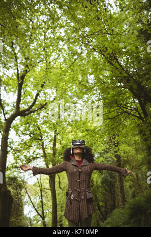 Woman with arms outstretched wearing virtual reality headset at forest Stock Photo