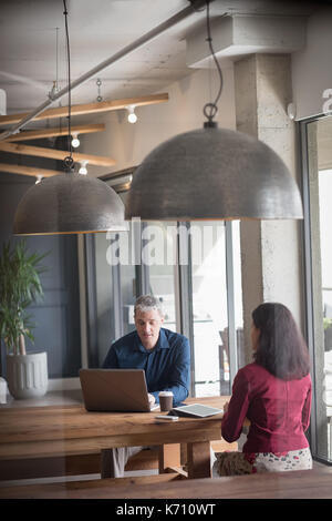 Businessman discussing with colleague while using laptop at table Stock Photo