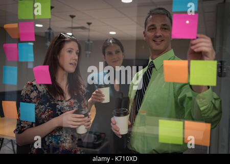 Business colleagues discussing over sticky notes seen through glass in office Stock Photo
