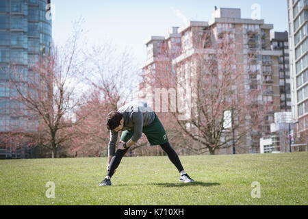 Full length of man doing stretching exercise on field against buildings Stock Photo