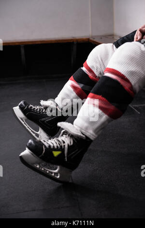 Low section of male hockey player wearing ice skates relaxing in dressing room Stock Photo