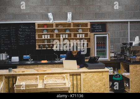 Male owner using laptop while standing at bar counter in cafe Stock Photo