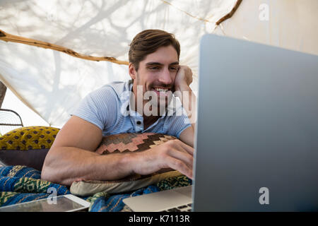 Happy young man using laptop while lying down in tent Stock Photo