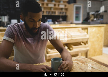 Thoughtful young man with coffee cup sitting at table in cafe Stock Photo