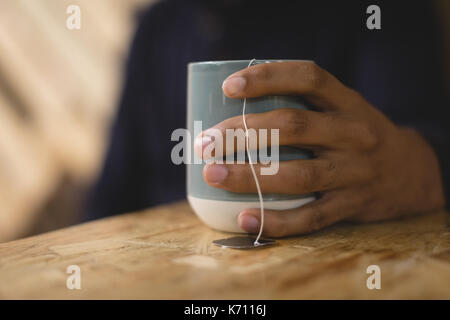 Cropped hand of young man holding tea cup while sitting at table in cafe Stock Photo