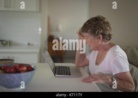 Tense senior woman using laptop in kitchen at home Stock Photo