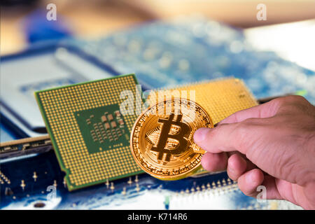 Hand holding a bitcoin and blurred computer processors in the background Stock Photo
