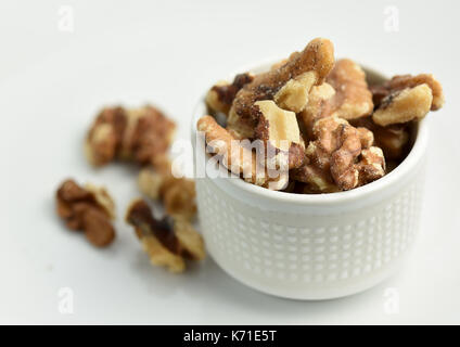 Close-up on a little white bowl with walnuts broken in pieces Stock Photo