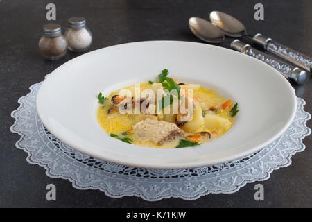 Creamy soup with fish fillet and mussels in a white plate on a white cloth on a grey abstract background. Healthy eating concept. Meditteranean lifestyle Stock Photo