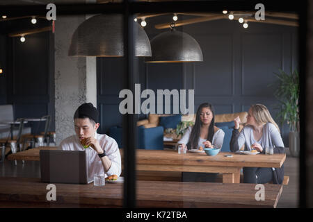 Businessman using laptop with colleagues discussing at table seen through glass in office cafeteria Stock Photo