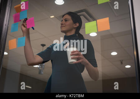 Businesswoman writing on sticky note seen through glass in office Stock Photo