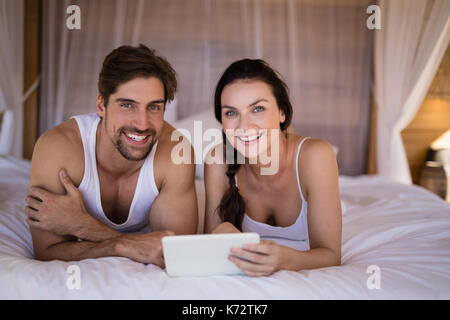 Portrait of smiling couple using digital tablet on bed in cottage Stock Photo