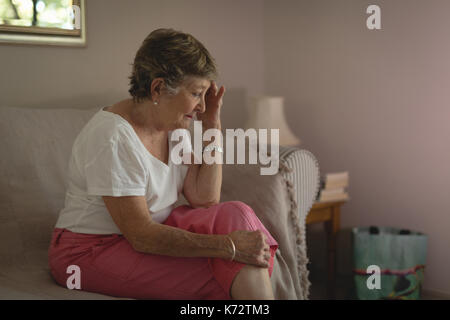 Tense senior woman sitting on sofa in living room at home Stock Photo