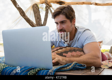 Young man using laptop while lying down in tent Stock Photo