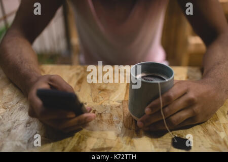 High angle midsection of young man with tea cup using mobile phone while sitting in cafe Stock Photo