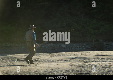 Side view of man with fishing rod while kneeling on riverbank during sunny day Stock Photo