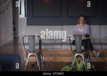 Full length of businesswoman using tablet on sofa in office cafeteria Stock Photo